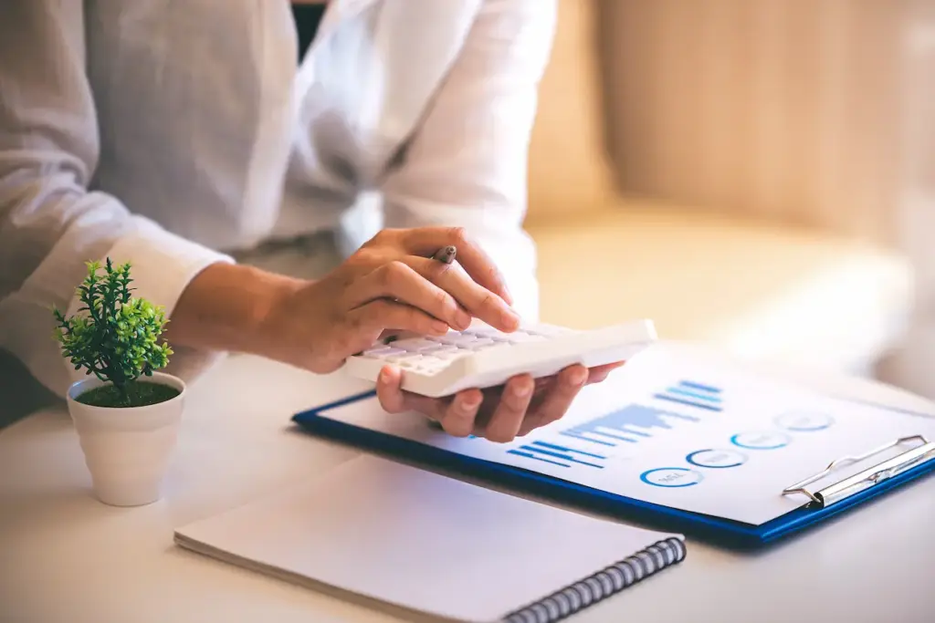 A person using a calculator next to a clipboard with charts and a small potted plant, representing bookkeeping services in Kissimmee.