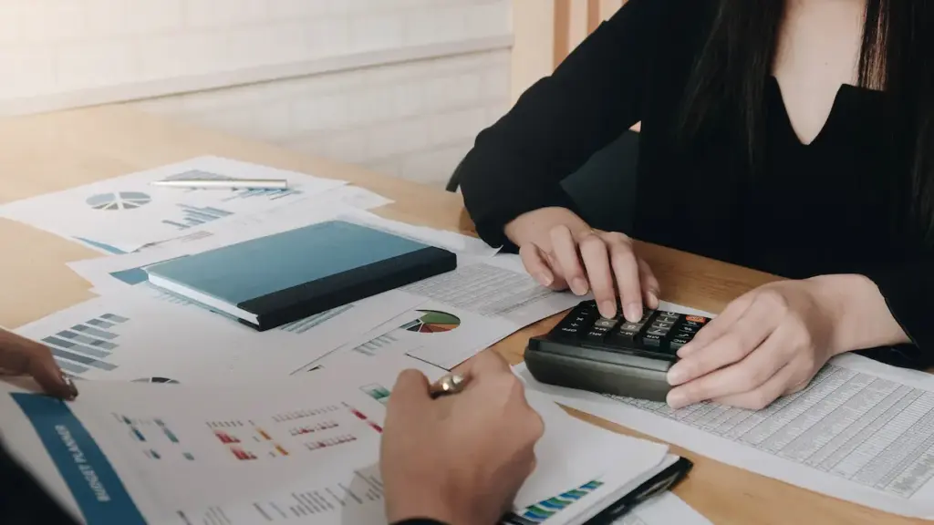 Two people using a calculator and reviewing financial documents at a wooden table for bookkeeping cleanup services.