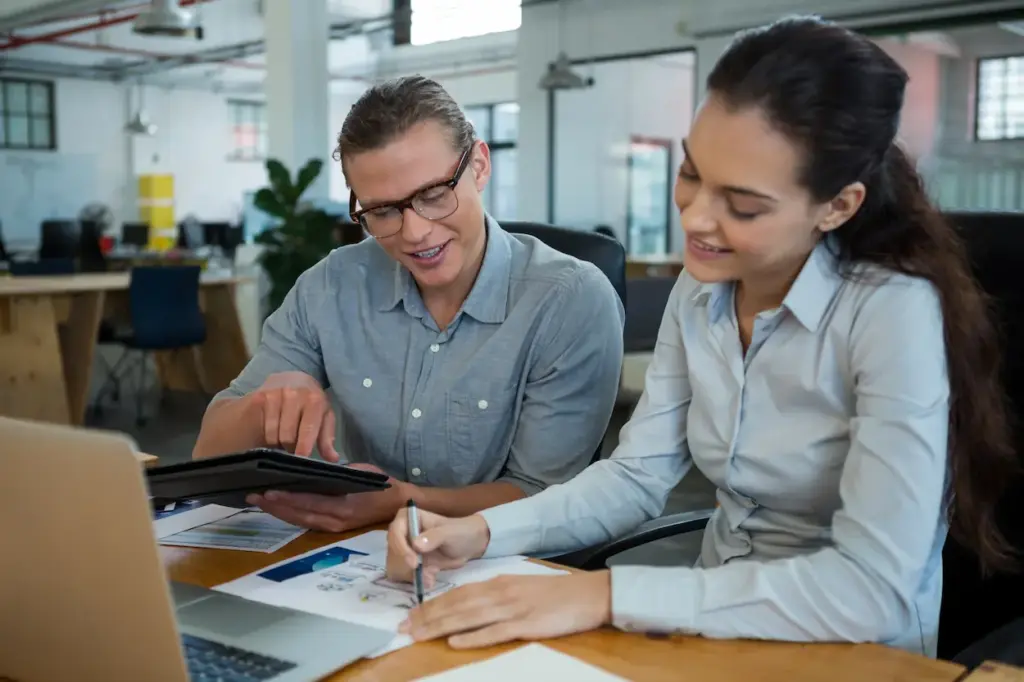 An Orlando FL bookkeeper and a woman sit at a desk collaborating on a project with a tablet and documents.