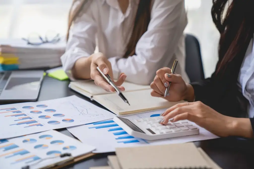Two people reviewing construction bookkeeping charts and using a calculator at a desk.