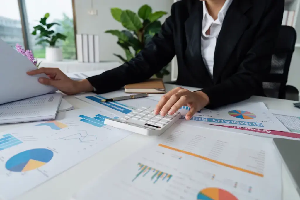 A person in a business suit working at a desk with financial charts, a calculator, and a food truck bookkeeping report.