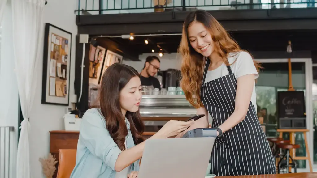 A customer pays for her coffee at a food truck by tapping her smartphone on a card reader held by a smiling barista.