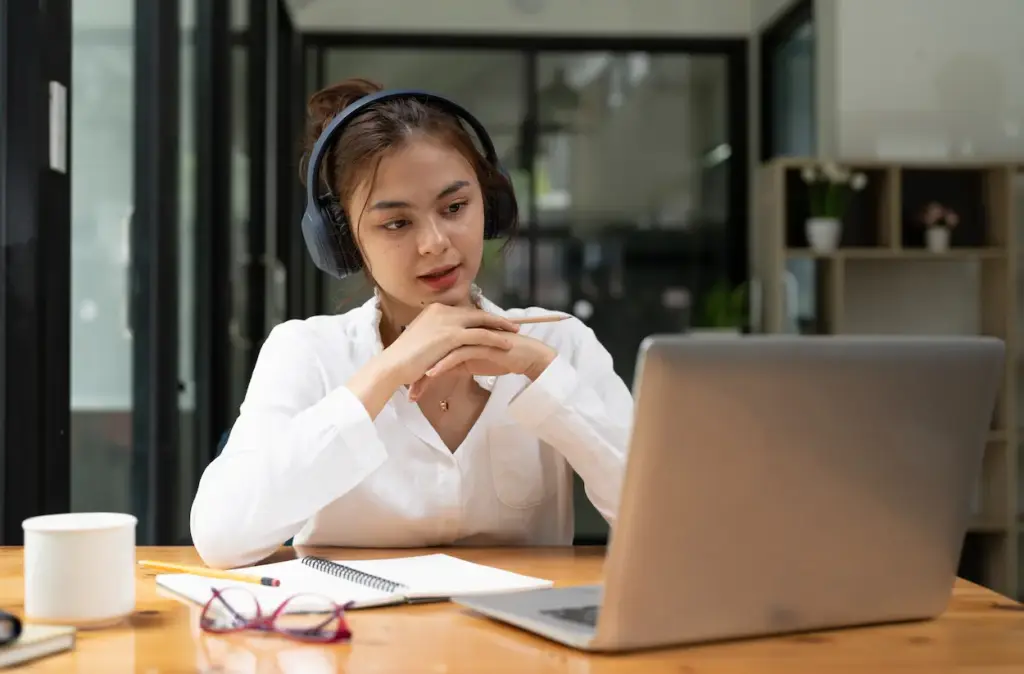 A woman wearing headphones sits at a desk looking at a laptop with an open notebook and pencil in hand while managing bookkeeping services in Kissimmee.