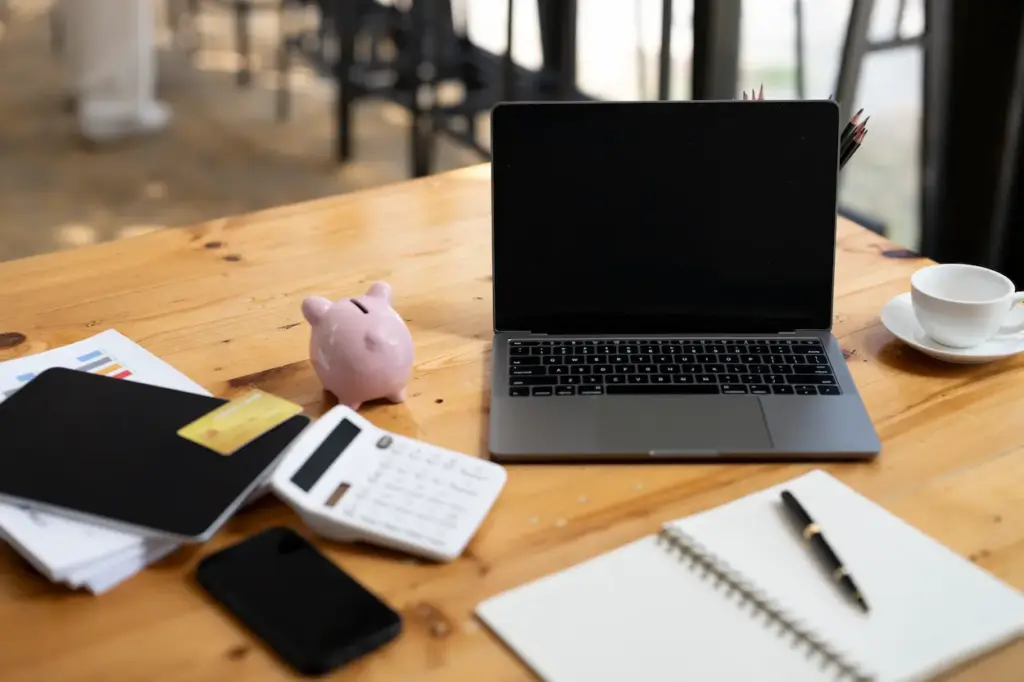 A wooden desk with a laptop, calculator, piggy bank, smartphone, notebook, pen, and coffee cup, typical of a bookkeeping service in Tampa.