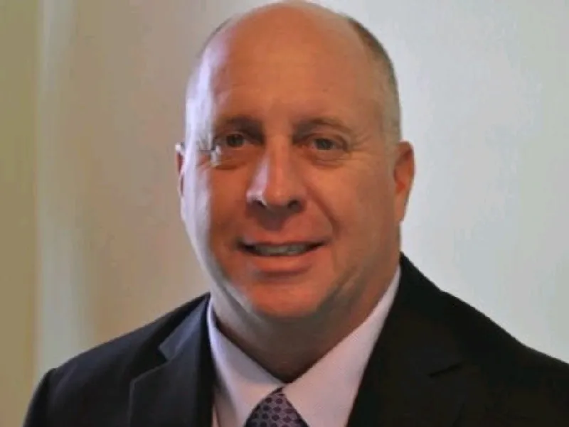 Headshot of a middle-aged Kraken Bookkeeping professional with a shaved head, wearing a dark suit, light shirt, and patterned tie.